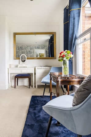 Classic design room with a vanity, mirror, and dresser, plus a comfortable armchair and wooden chair.