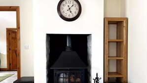 Een woonkamer met een zwarte haard, een houten plank en een klok aan de muur.
