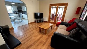 Een woonkamer met een houten vloer, een zwarte leren bank, een houten salontafel en een televisie.