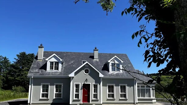 Een tweelaags huis met een rode deur, witte details en een grijs dak.