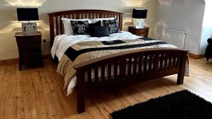 Een slaapkamer met een houten bed, twee nachtkastjes met lampen, een radiator en een zwart tapijt.