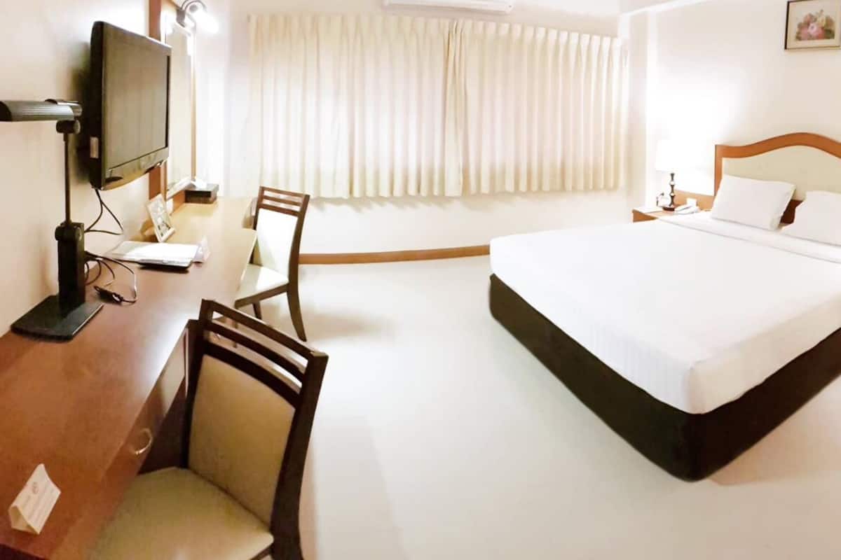 Ein Hotelzimmer mit Bett, Schreibtisch mit Computer, Stuhl, Fernseher und einem Fenster mit Vorhängen.
