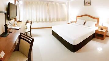 Habitación de hotel con cama, escritorio con computadora, silla, televisor y ventana con cortinas.