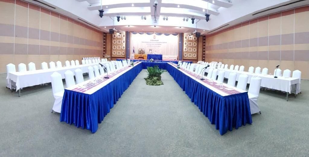 A conference room with a long table, white chairs, and a stage at the front.
