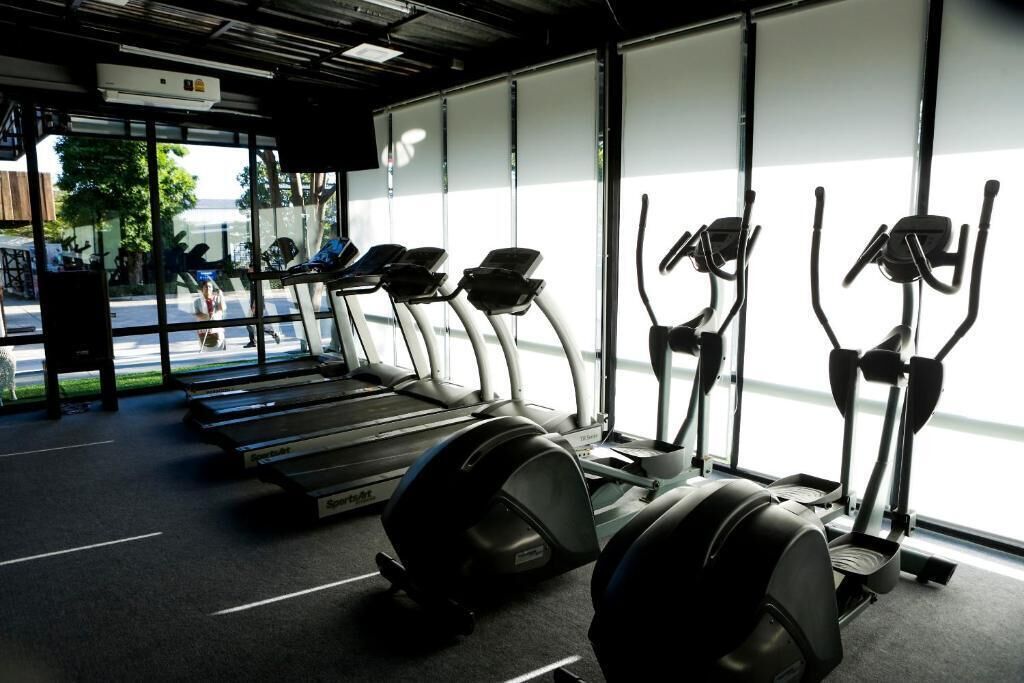 A gym with treadmills and elliptical machines, large windows, and a view of the street outside.