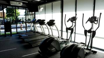 A gym with treadmills and elliptical machines, large windows, and a view of the street outside.