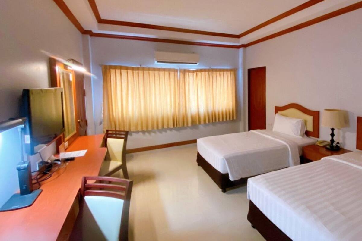 Ein Hotelzimmer mit zwei Betten, einem Schreibtisch mit Computer, einem Fernseher und einem Fenster mit Vorhängen.