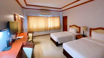 A hotel room with two beds, a desk with a computer, a TV, and a window with curtains.