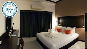 A DELUXE ROOM in the MAJOR GRAND HOTEL with a neatly made bed, a desk with a chair, and a large window with curtains. - Major Grand Hotel (Chum Phae)
