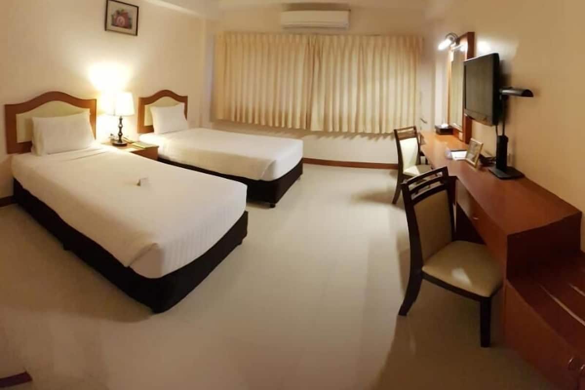 Ein Hotelzimmer mit zwei Betten, einem Schreibtisch mit Stuhl, einem Fernseher und einem Fenster mit Vorhängen.