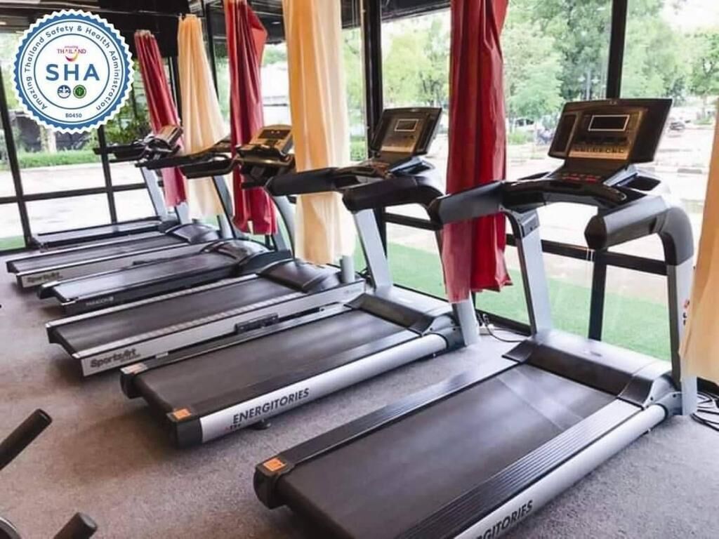 A row of treadmills with digital displays, arranged in a gym with large windows and curtains.