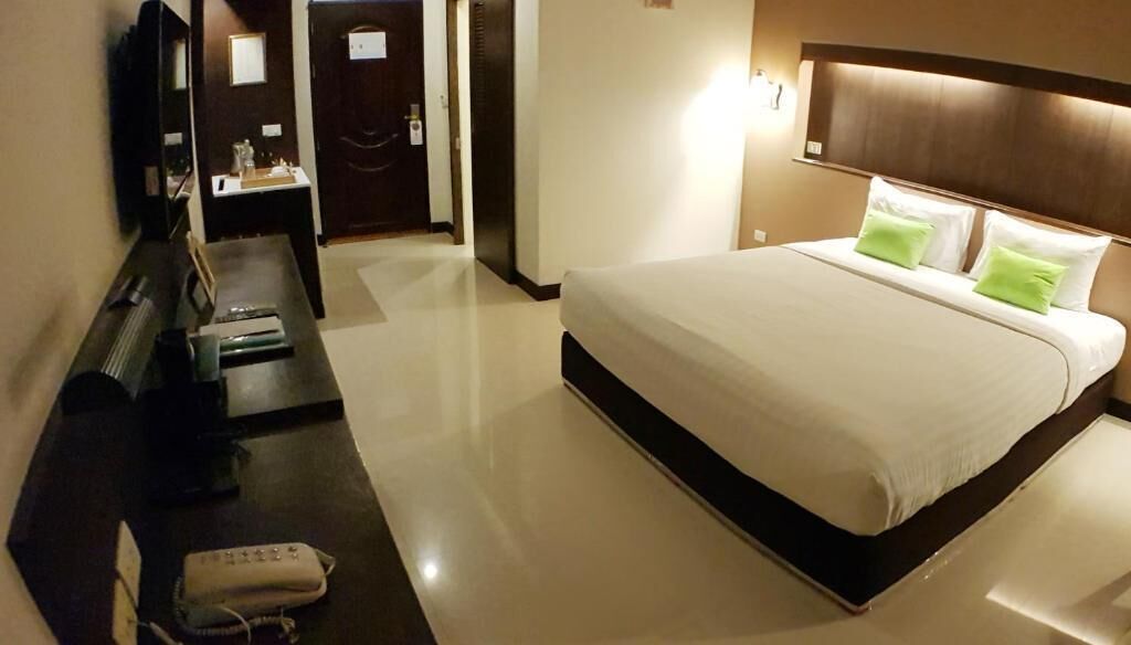 A hotel room with a large bed, a desk with a chair, a TV, and a bedside table with a lamp.