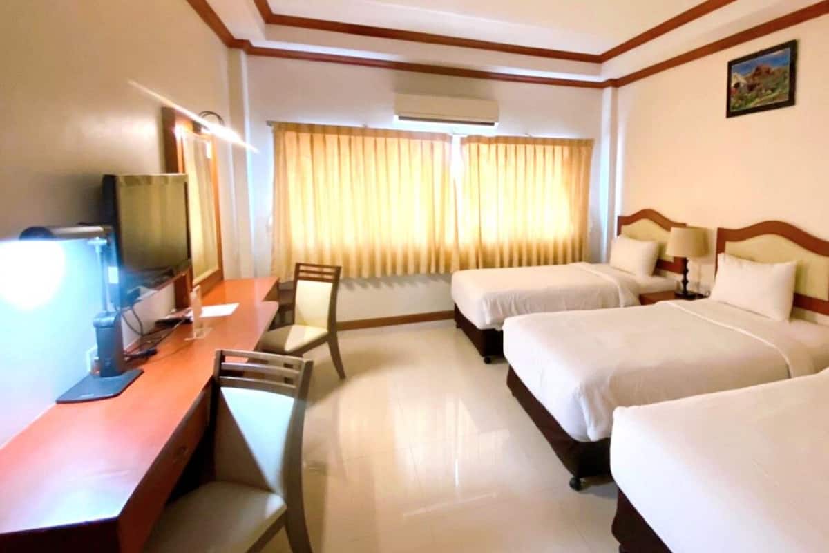 Ein Hotelzimmer mit zwei Betten, einem Schreibtisch mit Computer, einem Stuhl und einem Fenster mit Vorhängen.