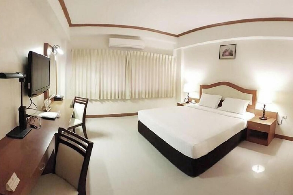 A hotel room with a bed, a desk with a chair, a television, and a window with curtains.
