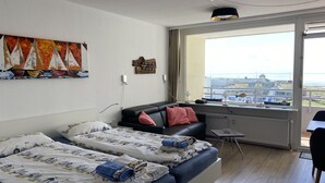 Hotellihuone, jossa on kaksi sänkyä, sohva, pieni pöytä ja näkymä lentokentälle.