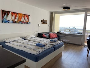 Habitación de hotel con dos camas, un sofá, una ventana con vistas y un cuadro en la pared.
