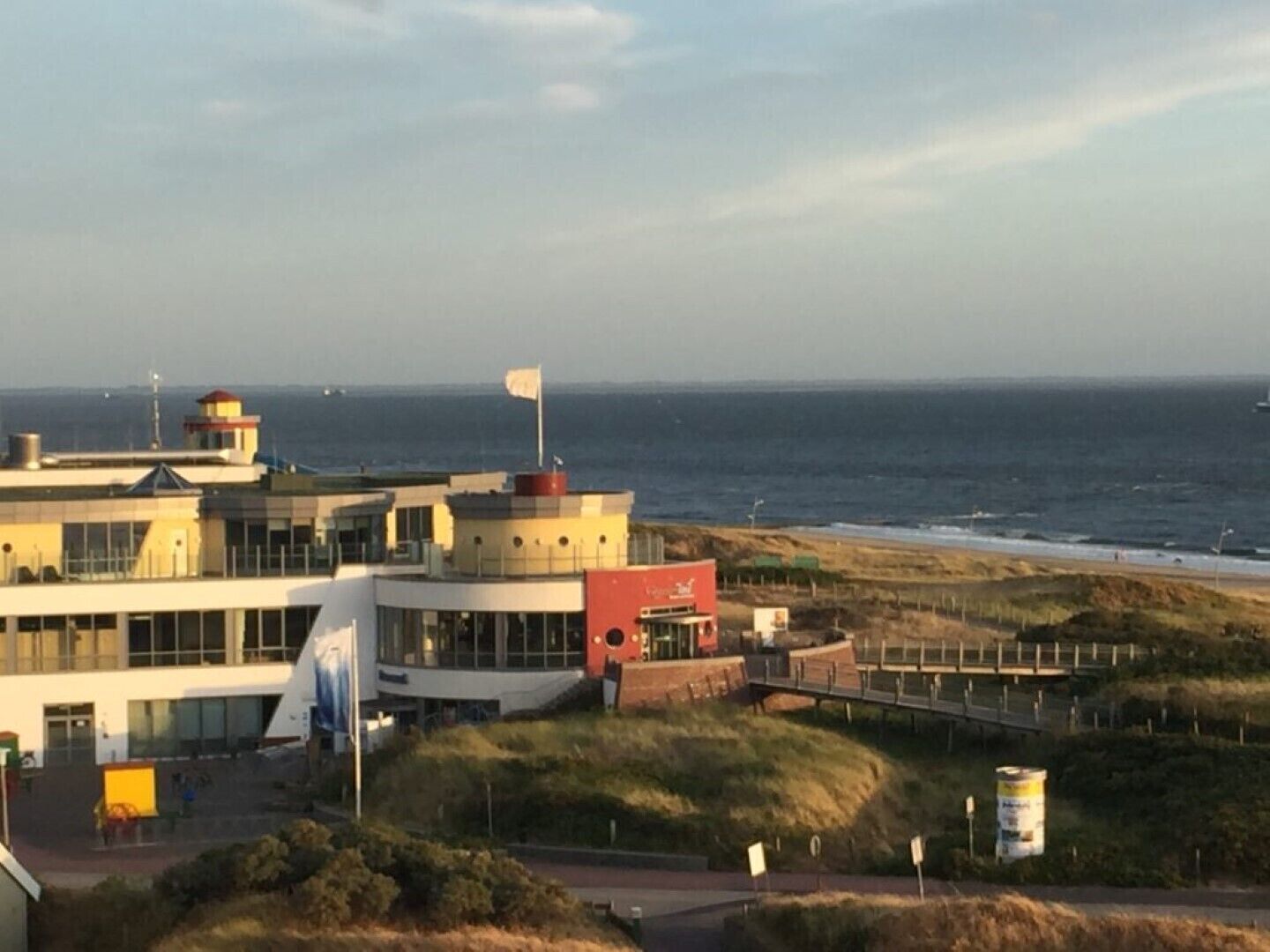 Ein Küstengebäude mit einer Flagge auf dem Dach, ein Strand im Hintergrund und ein klarer Himmel.