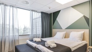 A hotel room with a large bed, a bench, and a view of the city through the window.