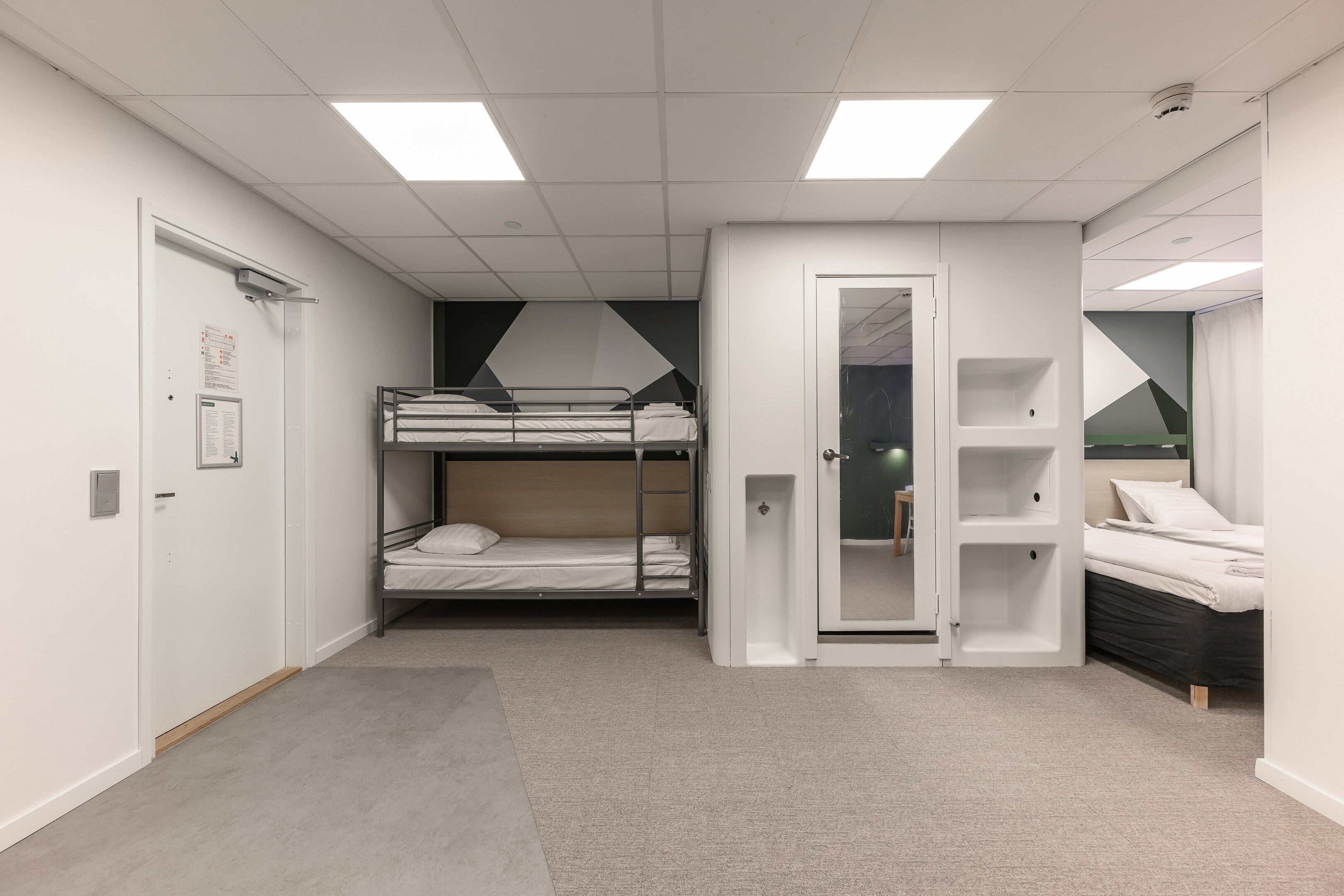 Une chambre moderne et bien éclairée, équipée de lits superposés, d’une armoire et d’un petit coin salon.