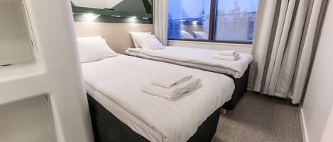 Habitación de hotel con dos camas, un ventanal con cortinas y un diseño moderno.