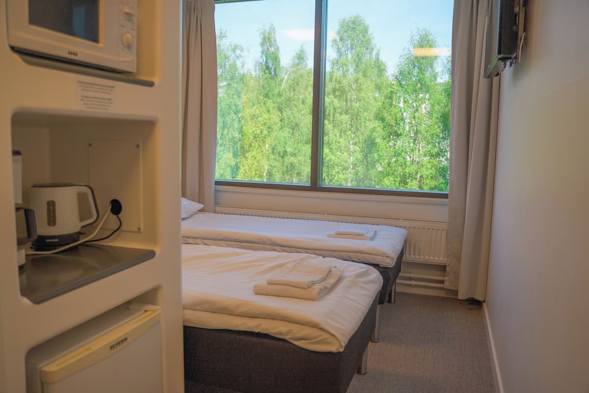 Een hotelkamer met twee bedden, een magnetron en een raam met uitzicht op bomen.
