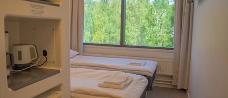 A hotel room with two beds, a microwave, and a window with a view of trees.