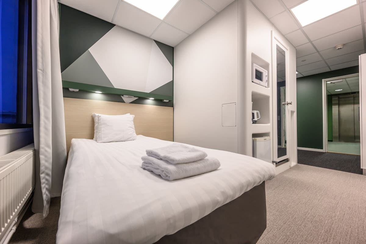Een hotelkamer met een bed, een nachtkastje, een spiegel en een deur naar een badkamer.