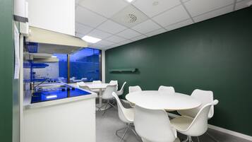 Un salón de conferencias con una mesa y sillas blancas, un área de hidratación azul y una pared verde.
