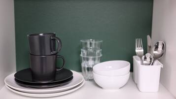 Una taza negra sobre una pila de platos blancos, una copa de cristal transparente, un cuenco blanco y un utensilero blanco con cubiertos.