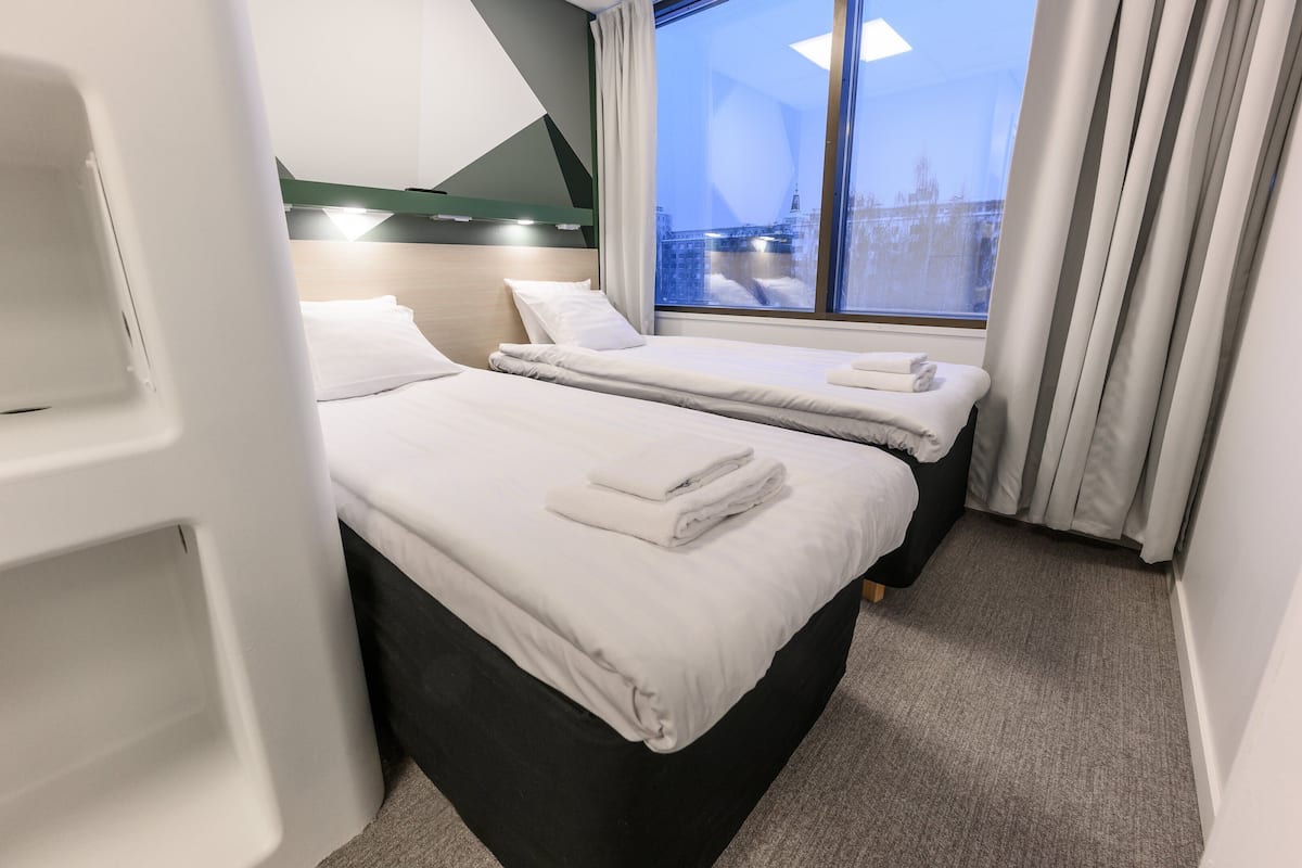 Een hotelkamer met twee bedden, een groot raam met gordijnen en uitzicht op een brug.