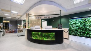 A reception area with a reception desk, a green wall with plants, and a sign indicating the reception.