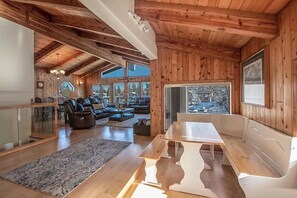 Een houten interieur met een eethoek, zitplaatsen en grote ramen.