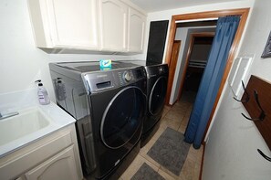 Een kleine wasruimte met een wasmachine, droger, wasbak en een klein kastje.