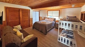 Un dormitorio acogedor con techo de madera, una cama grande, un sofá y un mueble de almacenamiento blanco.