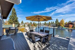 A deck with a table and chairs, a grill, and a view of a lake with boats. - Waterfront Home on Double Lot - Boat Dock, Hot Tub and More! (South Lake Tahoe)