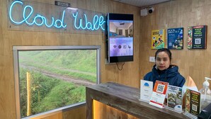 A reception desk with a neon sign reading "Cloud Walk," a digital screen displaying room information, and various informational posters. - Dolphin Nose Retreat (Kodaikanal)