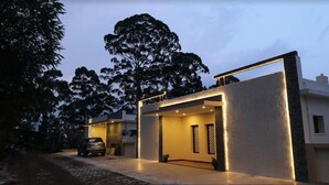 A modern house with a garage, a car parked outside, and a tree in the background. - Dolphin Nose Retreat (Kodaikanal)