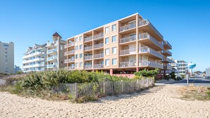 A multi-story hotel with balconies, located near a beach.