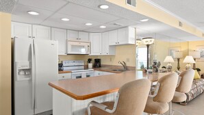 A modern kitchen with white cabinets, a built-in microwave, a refrigerator, and a central island with bar stools.