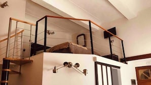 Un escalier avec une rampe en métal menant à une mezzanine dotée d’un plafond en bois.
