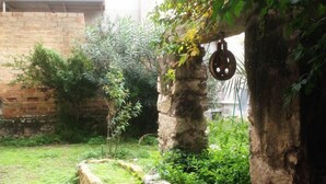 Un jardin rustique avec des murs en pierre, un pot suspendu et un petit arbre.