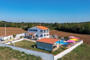 Une maison à deux étages avec une piscine et des parasols d’extérieur.