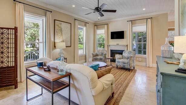 A spacious living room with a ceiling fan, large windows, a fireplace, and a television mounted on the wall. - 1016 San Fernando Street 3 Bedroom Home by RedAwning (Fernandina Beach)
