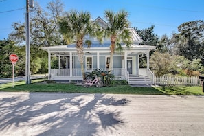 Two-story house with a gabled roof and porch, surrounded by a picket fence.