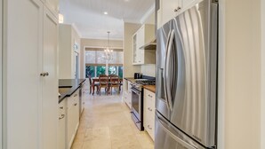 A modern kitchen with stainless steel appliances, white cabinetry, and a dining area with wooden chairs. - 1016 San Fernando Street 3 Bedroom Home by RedAwning (Fernandina Beach)