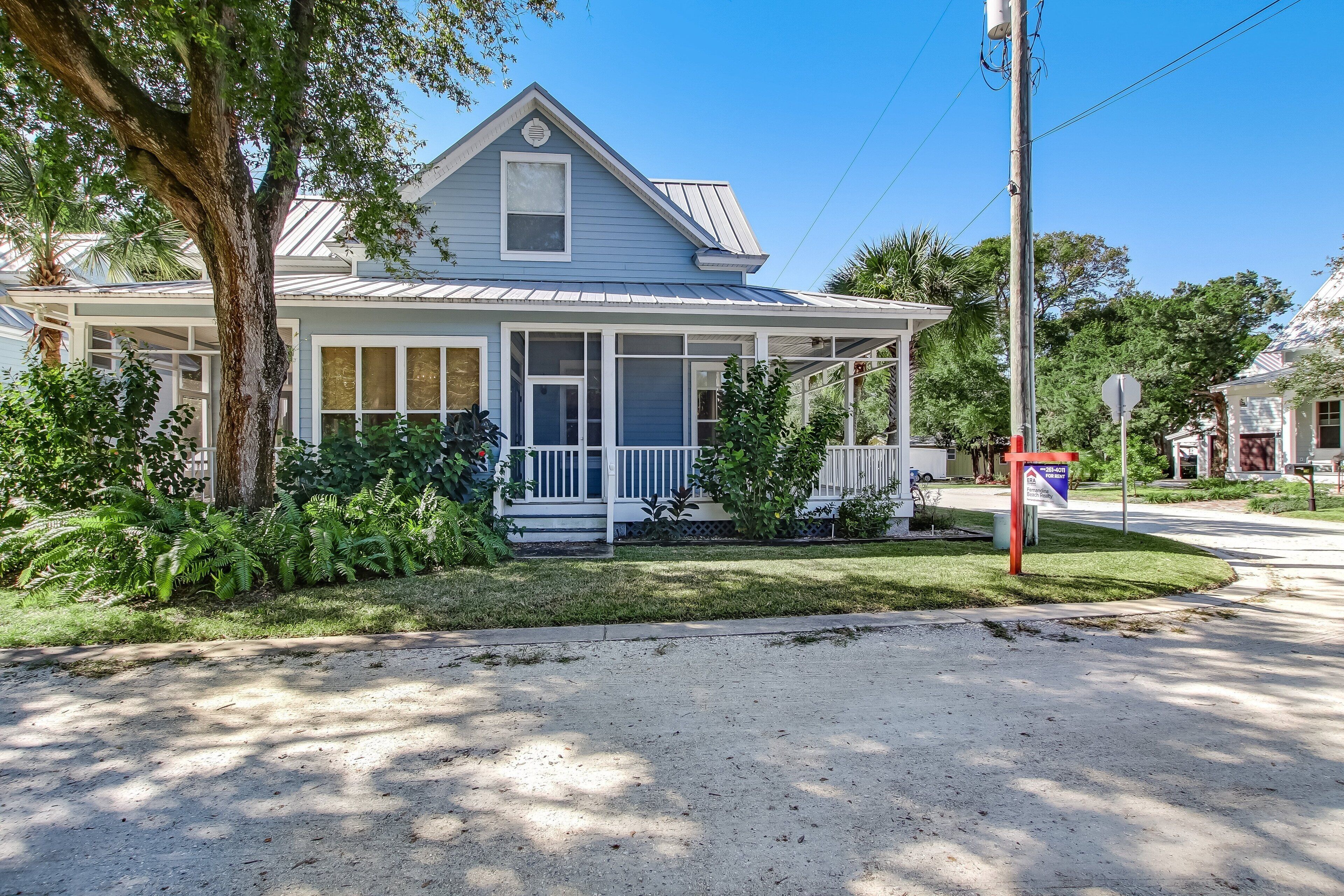 A two-story house with a porch, surrounded by greenery and a clear sky.