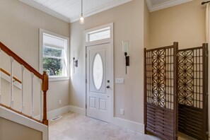 Stunning hallway with a white door, window, and decorative gate, set against a light-colored tile floor and wooden staircase.