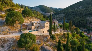 Une maison en pierre avec une piscine, entourée d’arbres et de collines.