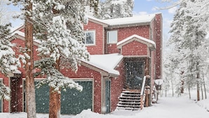 Una casa de ladrillo rojo con una puerta de garaje verde, rodeada de árboles cubiertos de nieve.