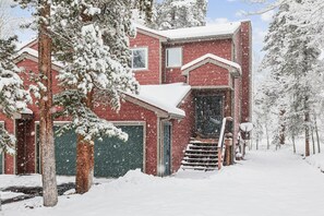 Une maison en briques rouges avec une porte de garage verte, entourée d’arbres couverts de neige.